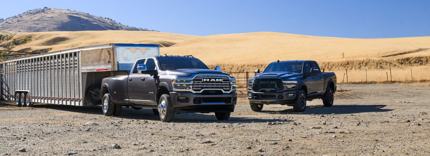 Two Ram pickups on a cattle ranch. On the left, a gray Ram 3500 Laramie Crew Cab towing a large fifth-wheel livestock trailer, and on the right, a black Ram 2500 Rebel Crew Cab.